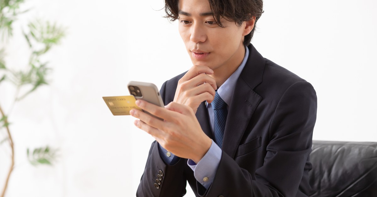 クレジットカードとスマートフォンを持つスーツ姿の男性